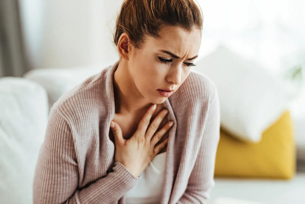 a woman sitting on the sofa with her hand on her chest due to acid reflux discomfort. acid reflux treatment in Huddersfield.